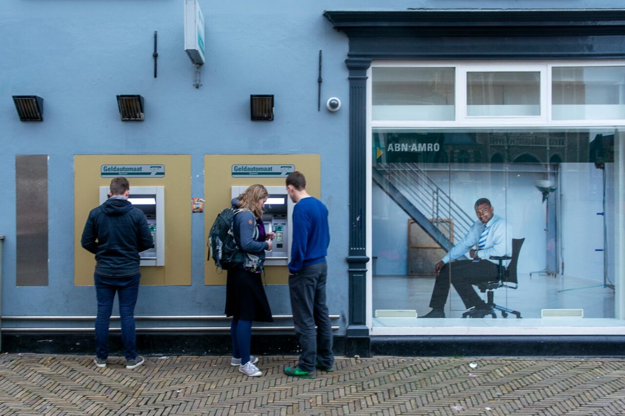 people standing at the atm machines in a wall of a building in city